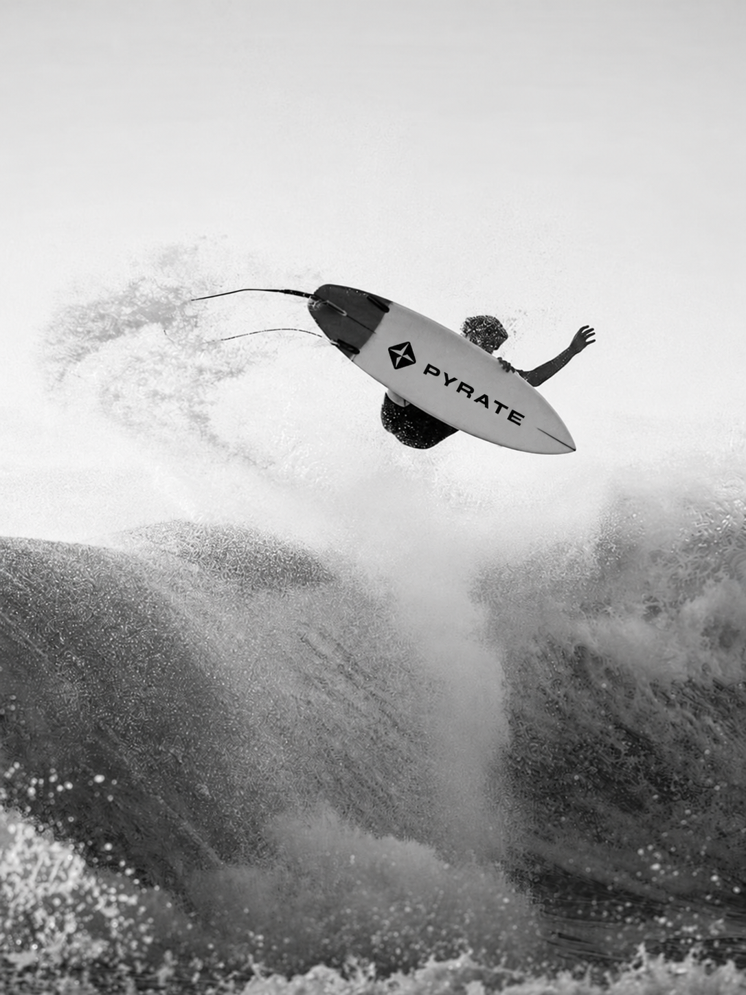 Surfer performing an aerial above a wave on a PYRATE-branded board, in black and white.
