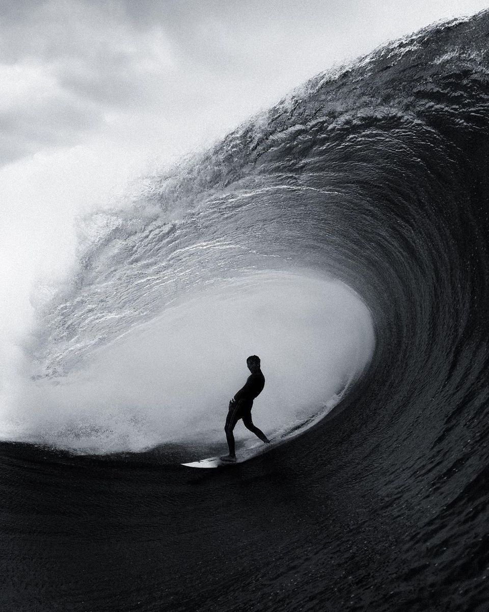 Surfer riding inside a large barreling wave in black and white.