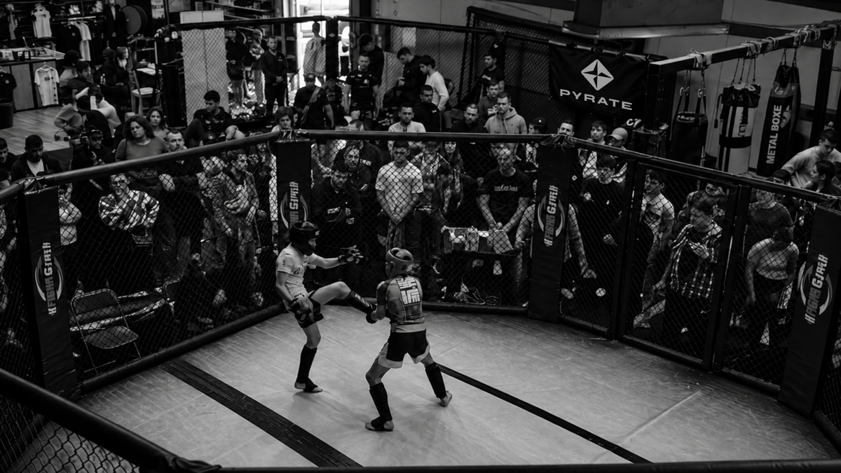 Fighters sparring in an MMA cage with a PYRATE banner in the gym